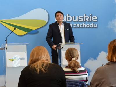 Widok sali podczas konferencji prasowej, obejmujący dziennikarzy oraz uczestnika konferencji przy mównicy.
