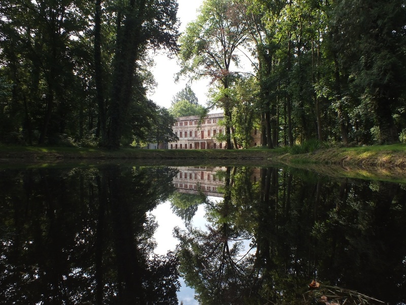 Zatonie. Fotografia, w swojej centralnej części przedstawia ruiny pałacu znajdującego się w Parku Książęcym Zatonie, który założony został w XIX w. Zaprojektował go wybitny niemiecki projektant - Peter Lenné , z polecenia księżnej Doroty de Talleyrand-Périgord. Widok dawnej rezydencji wraz z pobliskimi roślinami, odbija się w tafli Wielkiego Stawu (znajdującego się na terenie Parku), dzięki czemu powstał ciekawy efekt „symetrycznego” obrazu. Zatonie stanowi część Zielonej Góry