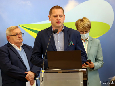 Konferencja prasowa Zarządu Województwa Lubuskiego dotycząca projektu budżetu na 2022 rok. Przy mikrofonie wicemarszałek Łukasz Porycki. Z tyłu od lewej stoją członek zarządu Tadeusz Jędrzejczak oraz marszałek Elżbieta Anna Polak.