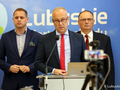 Konferencja prasowa Zarządu Województwa Lubuskiego dotycząca projektu budżetu na 2022 rok. Przy mikrofonie członek zarządu Marcin Jabłoński. Z tyłu od lewej stoją: wicemarszałkowie Łukasz Porycki oraz Stanisław Tomczyszyn.