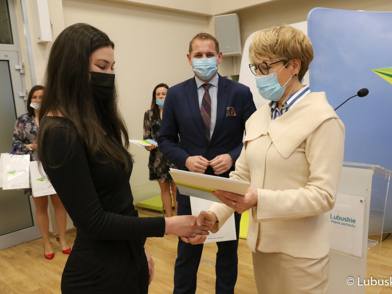 Marszałek Elżbieta Anna Polak oraz wicemarszałek Łukasz Porycki wręczają studentce stypendium motywujące