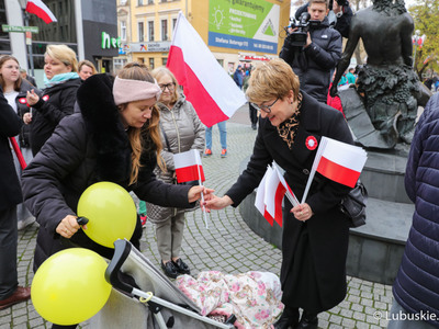 Marszałek Województwa Lubuskiego Elżbieta Anna Polak rozdaje biało-czerwone chorągiewki uczestnikom Marszu Niepodległości w Zielonej Górze