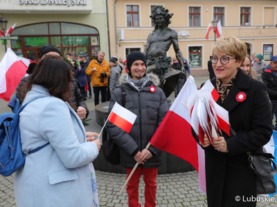 Marszałek Województwa Lubuskiego Elżbieta Anna Polak rozdaje biało-czerwone chorągiewki uczestnikom Marszu Niepodległości w Zielonej Górze