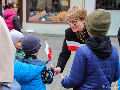 Marszałek Województwa Lubuskiego Elżbieta Anna Polak rozdaje biało-czerwone chorągiewki uczestnikom Marszu Niepodległości w Zielonej Górze