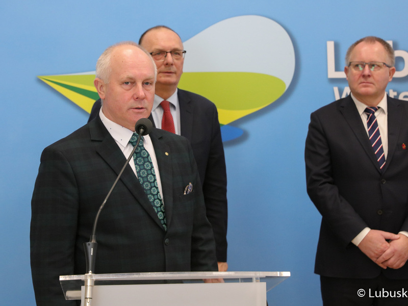 Radny Województwa Lubuskiego Zbigniew Kołodziej (przy mikrofonie) przemawia podczas konferencji prasowej na temat nawadniania boisk piłkarskich i programu trybuna. Z tyłu: Wicemarszałek Województwa Lubuskiego Stanisław Tomczyczyn oraz Członek Zarządu PZPN i Prezes LZPN Robert Skowron