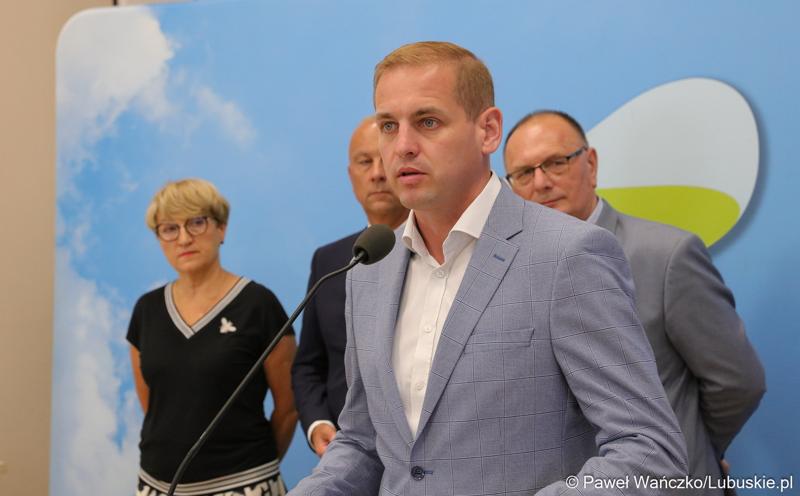 Wicemarszałek Województwa Lubuskiego Łukasz Porycki przemawia podczas konferencji prasowej. Z tyłu stoją (od lewej): Marszałek Województwa Lubuskiego Elżbieta Anna Polak, Członek Zarządu Województwa Lubuskiego Marcin Jabłoński oraz Wicemarszałek Województwa Lubuskiego Stanisław Tomczyszyn.