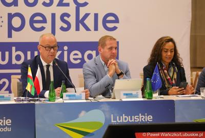 Stół prezydialny Komitetu Minitorującego Fundusze Europejskie dla Lubuskiego 2021-2027. Od lewej: Członek  Zarządu Województwa Lubuskiego Marcin Jabłoński, Wicemarszałek Województwa Lubuskiego Łukasz Porycki oraz Cinzia Masina, Zastępca Dyrektora Wydziału ds. Polski, Czech i Słowacji w Dyrekcji Generalnej ds. Zatrudnienia, Spraw Społecznych i Włączenia Społecznego Komisji Europejskiej 