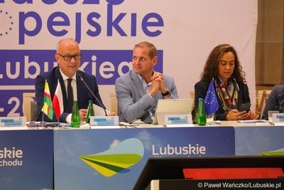 Stół prezydialny Komitetu Minitorującego Fundusze Europejskie dla Lubuskiego 2021-2027. Od lewej: Członek  Zarządu Województwa Lubuskiego Marcin Jabłoński, Wicemarszałek Województwa Lubuskiego Łukasz Porycki oraz Cinzia Masina, Zastępca Dyrektora Wydziału ds. Polski, Czech i Słowacji w Dyrekcji Generalnej ds. Zatrudnienia, Spraw Społecznych i Włączenia Społecznego Komisji Europejskiej 