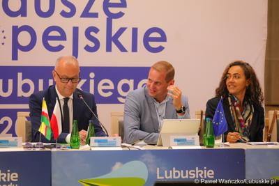 Stół prezydialny Komitetu Minitorującego Fundusze Europejskie dla Lubuskiego 2021-2027. Od lewej: Członek  Zarządu Województwa Lubuskiego Marcin Jabłoński, Wicemarszałek Województwa Lubuskiego Łukasz Porycki oraz Cinzia Masina, Zastępca Dyrektora Wydziału ds. Polski, Czech i Słowacji w Dyrekcji Generalnej ds. Zatrudnienia, Spraw Społecznych i Włączenia Społecznego Komisji Europejskiej 