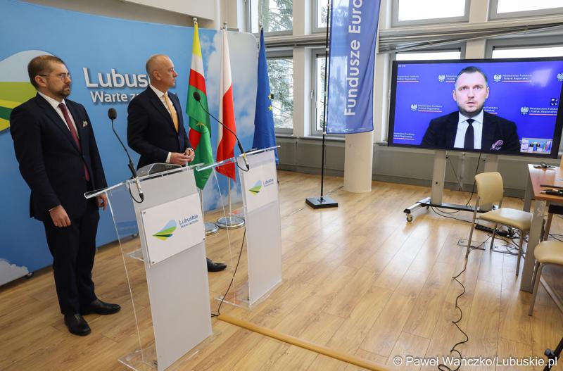 Marszałek Województwa Lubuskiego Marcin Jabłoński (w środku), dyrektor Zarządzający Pionem Funduszy Europejskich w Banku Gospodarstwa Krajowego Paweł Chorąży (z lewej) oraz podsekretarz stanu w Ministerstwie Funduszy i Polityki Regionalnej Konrad Wojnarowski (zdalnie na monitorze) podczas konferencji prasowej w urzędzie marszałkowskim w Zielonej Górze