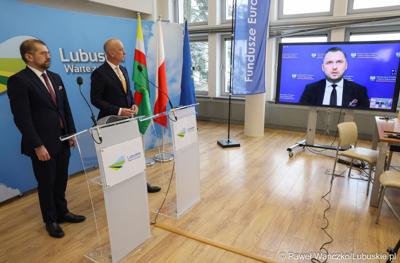 Marszałek Województwa Lubuskiego Marcin Jabłoński (w środku), dyrektor Zarządzający Pionem Funduszy Europejskich w Banku Gospodarstwa Krajowego Paweł Chorąży (z lewej) oraz podsekretarz stanu w Ministerstwie Funduszy i Polityki Regionalnej Konrad Wojnarowski (zdalnie na monitorze) podczas konferencji prasowej w urzędzie marszałkowskim w Zielonej Górze
