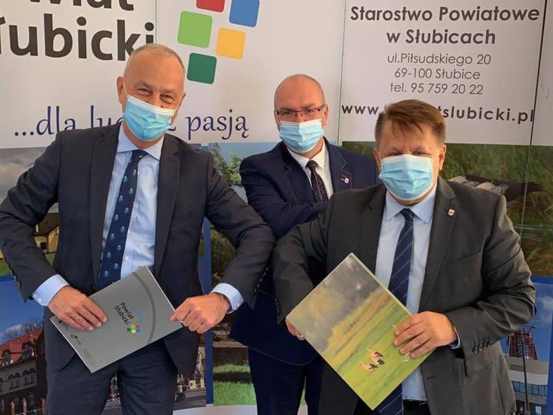 Trzy osoby, które podpisywały umowę, pozują na tle ścianki promocyjnej.