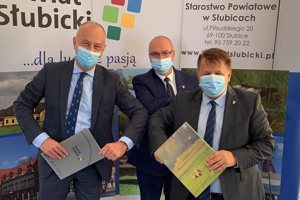Trzy osoby, które podpisywały umowę, pozują na tle ścianki promocyjnej.