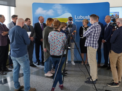 Uczestnicy konferencji prasowej i dziennikarze na tle ścianki z logiem województwa lubuskiego.