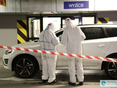 Dwie osoby w kombinezonach przy samochodzie.