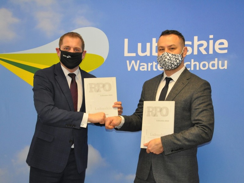 Dwie osoby trzymające podpisane umowy na stworzenie klubów seniora, stojące na tle ścianki promocyjnej z napisem "Lubuskie Warte Zachodu"