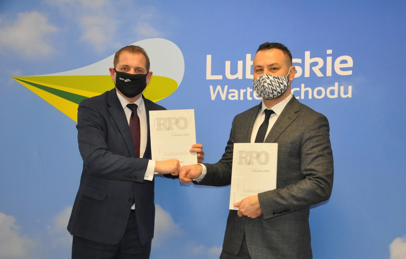 Dwie osoby trzymające podpisane umowy na stworzenie klubów seniora, stojące na tle ścianki promocyjnej z napisem 