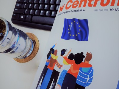 Zdjęcie przedstawia okładkę magazynu w centrum opartą o klawiaturę komputera w towarzystwie metalowego kubka.