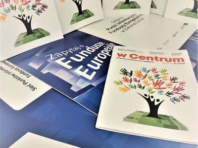 luźno ułożone gazety w centrum na tle plakatu, który promuje Punkty Informacyjne Funduszy Europejskich