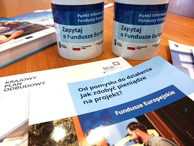 zdjęcie przedstawia 2 kubki z napisem punkty informacyjne funduszy europejskich. Są też ulotki o funduszach Unii Europejskiej i Krajowego Planu Odbudowy - KPO